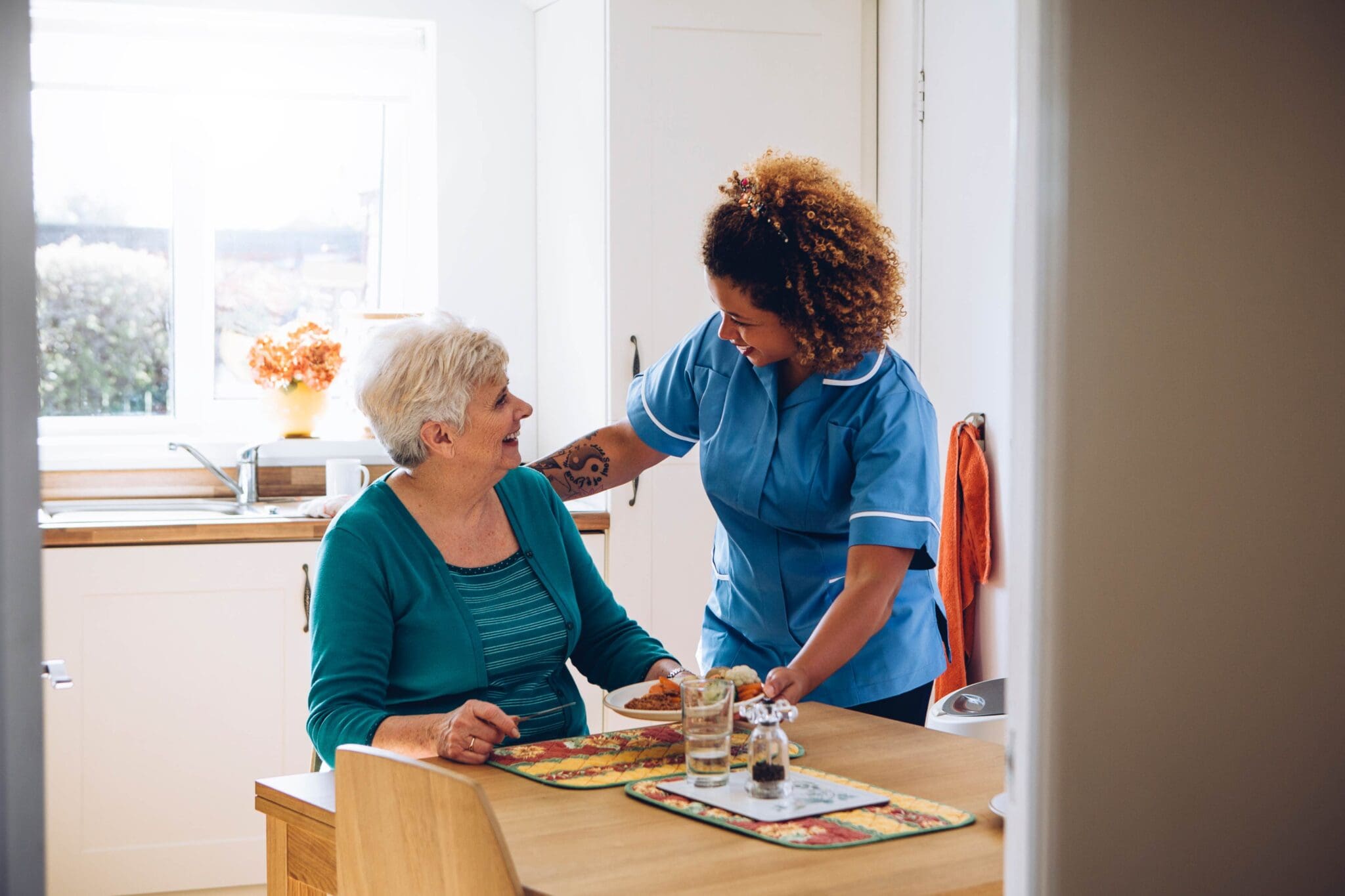 Caregiver serving elderly woman meal.
