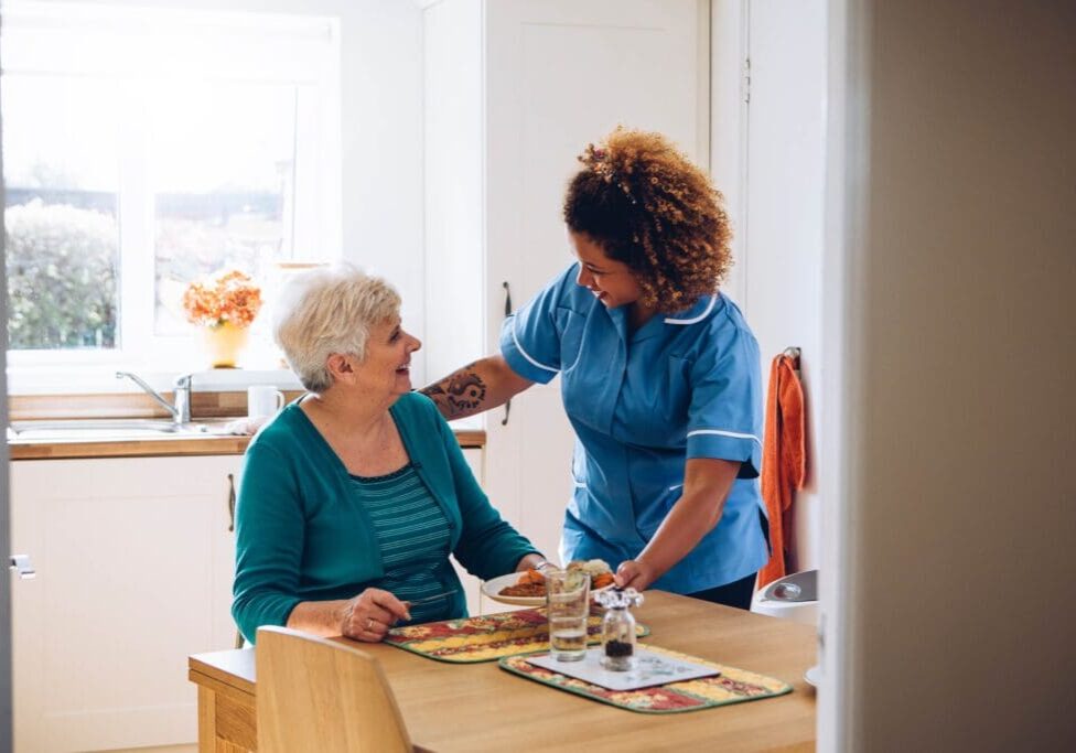 Caregiver serving elderly woman meal.