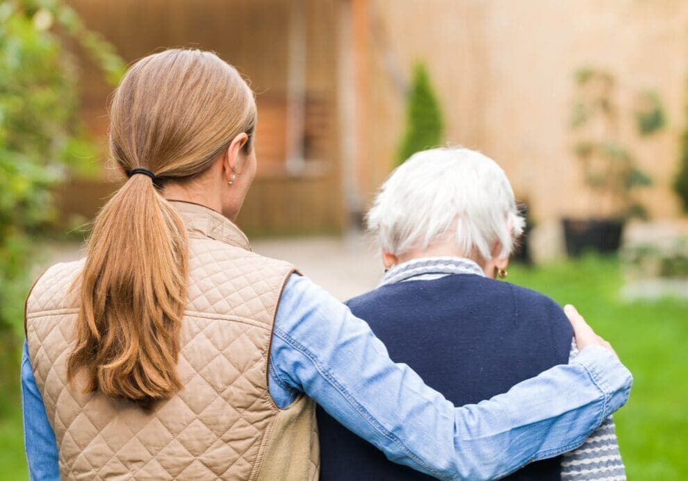 Woman supporting elderly person outdoors.